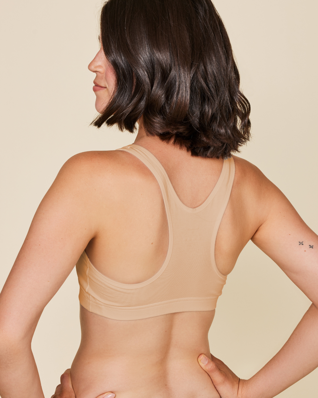 Woman wearing a beige bralette against a beige background