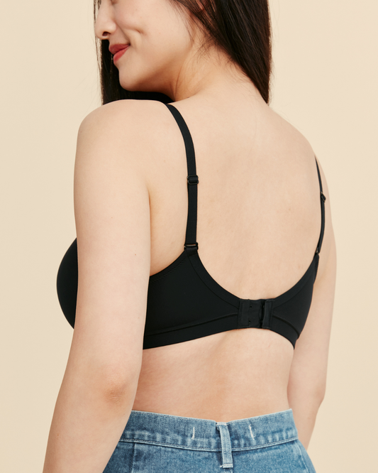 Woman wearing a black bralette with a beige background