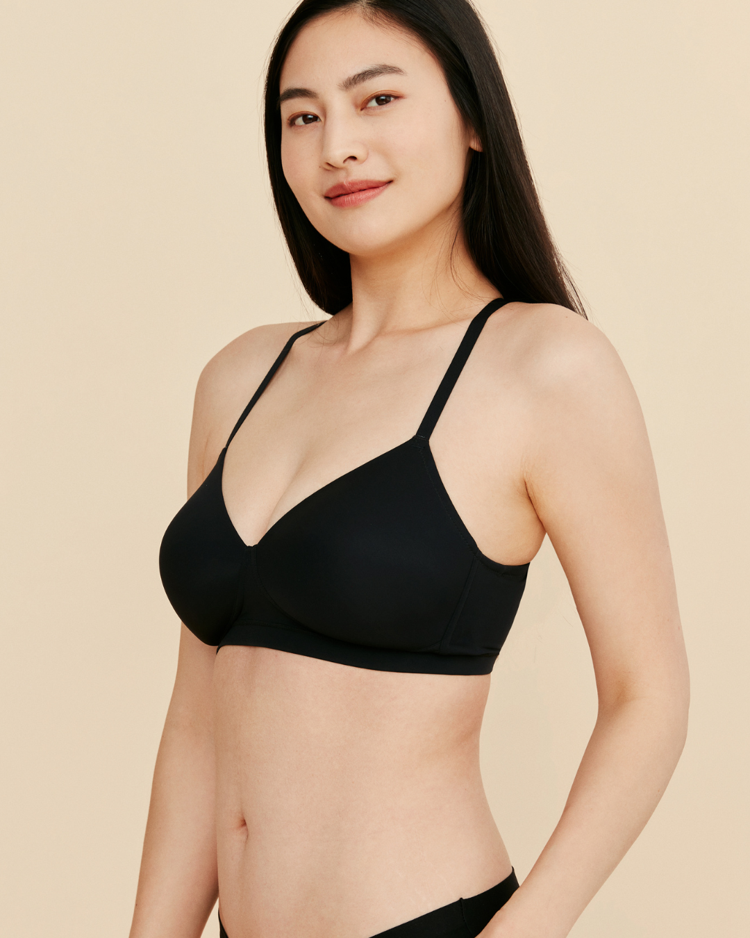 Woman wearing a black bralette against a beige background