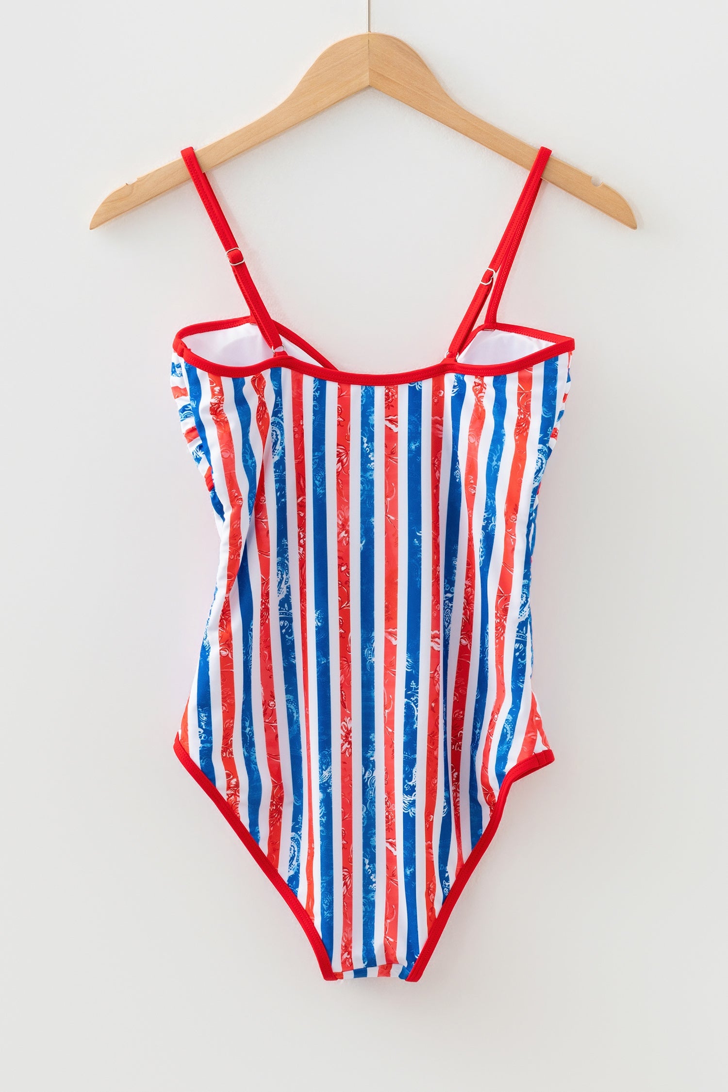 Striped swimsuit with red, white, and blue pattern on a hanger against a white background