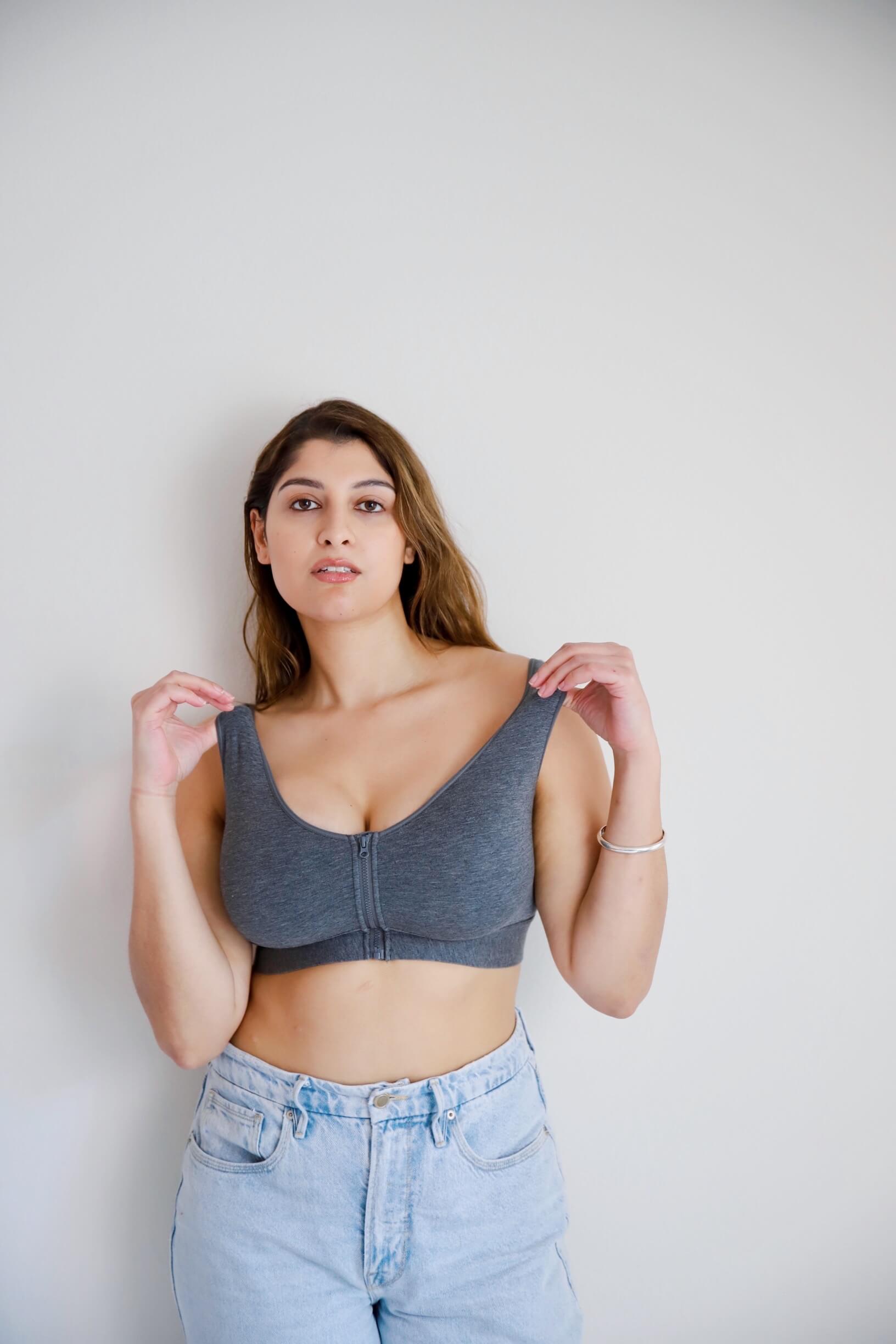 Woman wearing a gray bralette and light blue jeans against a plain background