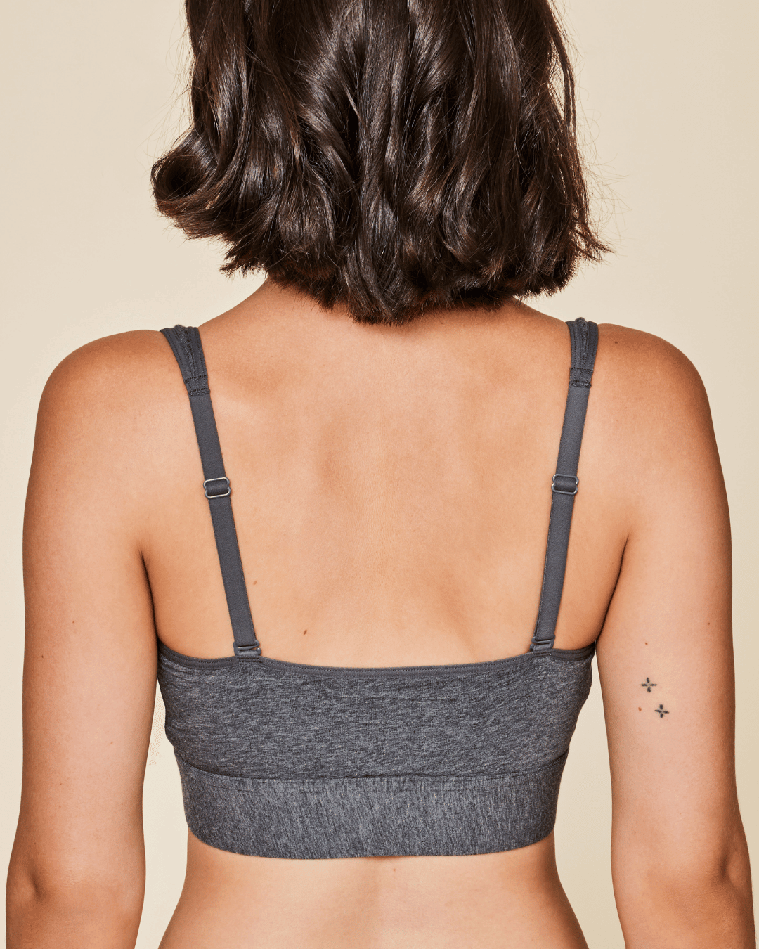 Person wearing a gray bralette on a beige background