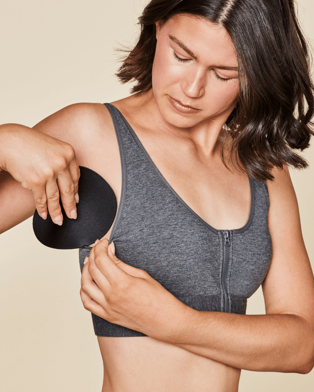 Woman wearing a gray sports bra holding a black arm sleeve against a beige background